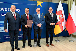 Marszałek Województwa Lubelskiego Jarosław Stawiarski pozuje do zdjęć z dwoma mężczyznami, beneficjentami projektu. Jeden z nich trzyma teczkę z umową. Obok nich stoi Dyrektor Wojewódzkiego Urzędu Pracy w Lublinie Tomasz Pitucha.