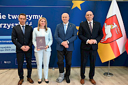 Marszałek Województwa Lubelskiego Jarosław Stawiarski pozuje do zdjęć z beneficjentami projektu, mężczyzna oraz kobieta trzymająca teczkę z umową. Obok nich stoi Dyrektor Wojewódzkiego Urzędu w Lublinie Pracy Tomasz Pitucha.
