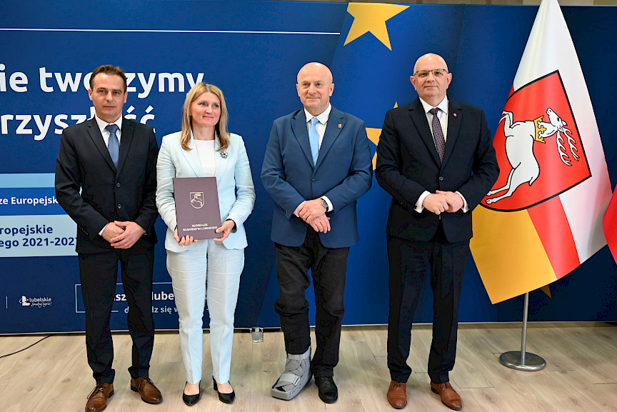 Marszałek Województwa Lubelskiego Jarosław Stawiarski pozuje do zdjęć z beneficjentami projektu, mężczyzna oraz kobieta trzymająca teczkę z umową. Obok nich stoi Dyrektor Wojewódzkiego Urzędu w Lublinie Pracy Tomasz Pitucha.
