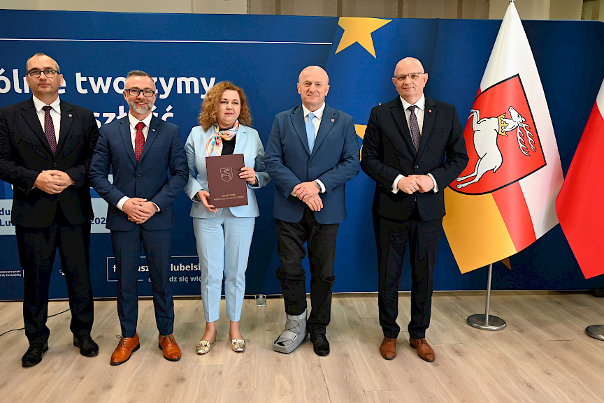 Marszałek Województwa Lubelskiego Jarosław Stawiarski pozuje do zdjęć z beneficjentami projektu, z dwoma mężczyznami oraz kobietą trzymającą teczkę z umową. Obok nich stoi Dyrektor Wojewódzkiego Urzędu w Lublinie Pracy Tomasz Pitucha.