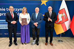 Marszałek Województwa Lubelskiego pozuje do zdjęć z beneficjentami projektu, mężczyzną oraz kobietą trzymającą teczkę z umową. Obok Marszałka stoi dyrektor Wojewódzkiego Urzędu Pracy w Lublinie Tomasz Pitucha.