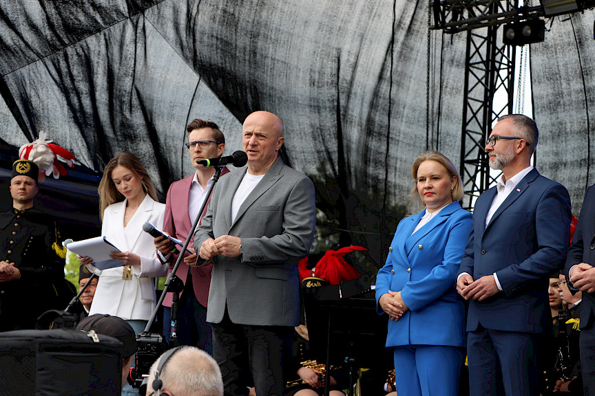 Marszałek Województwa Lubelskiego przemawia ze sceny. Obok niego stoi Dyrektor Anna Brzyska, Burmistrz Miasta Łęczna oraz prowadzący wydarzenie.