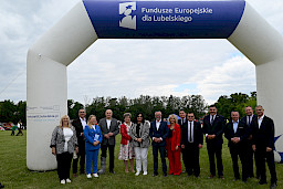 Grupa elegancko ubranych ludzi na tle bramy z napisem Fundusze Europejskie dla Lubelskiego.