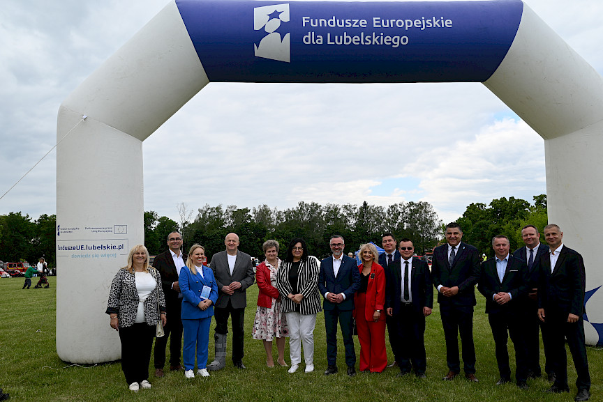 Grupa elegancko ubranych ludzi na tle bramy z napisem Fundusze Europejskie dla Lubelskiego.
