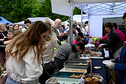 Tłum ludzi obok stoiska gastronomicznego - na pierwszym planie widoczne tace z poczęstunkiem.