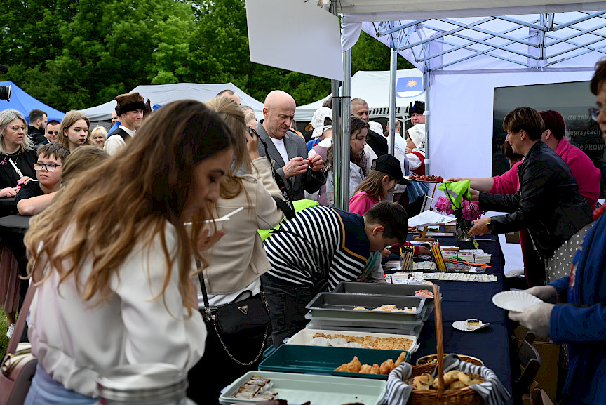 Tłum ludzi obok stoiska gastronomicznego - na pierwszym planie widoczne tace z poczęstunkiem.