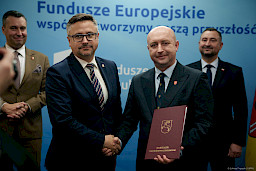 Wicemarszałek Województwa Lubelskiego Piotr Breś podaje rękę w ramach gratulacji beneficjentowi projektu, za nimi stoją inni Przedstawiciele Zarządu Województwa Lubelskiego.