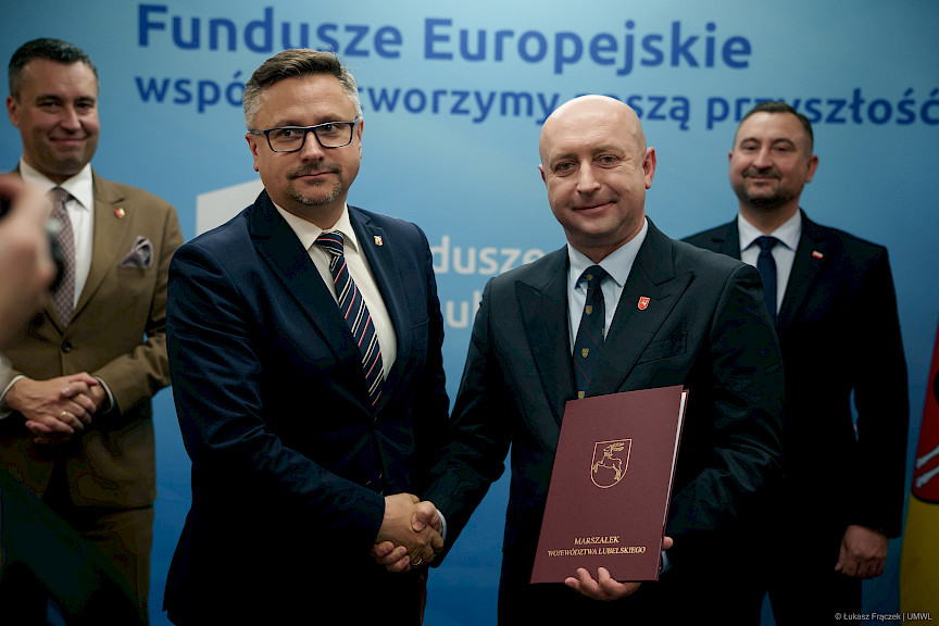 Wicemarszałek Województwa Lubelskiego Piotr Breś podaje rękę w ramach gratulacji beneficjentowi projektu, za nimi stoją inni Przedstawiciele Zarządu Województwa Lubelskiego.