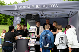 Stoisko Gminy Puchaczów i ludzie stojący za i przed stoiskiem.