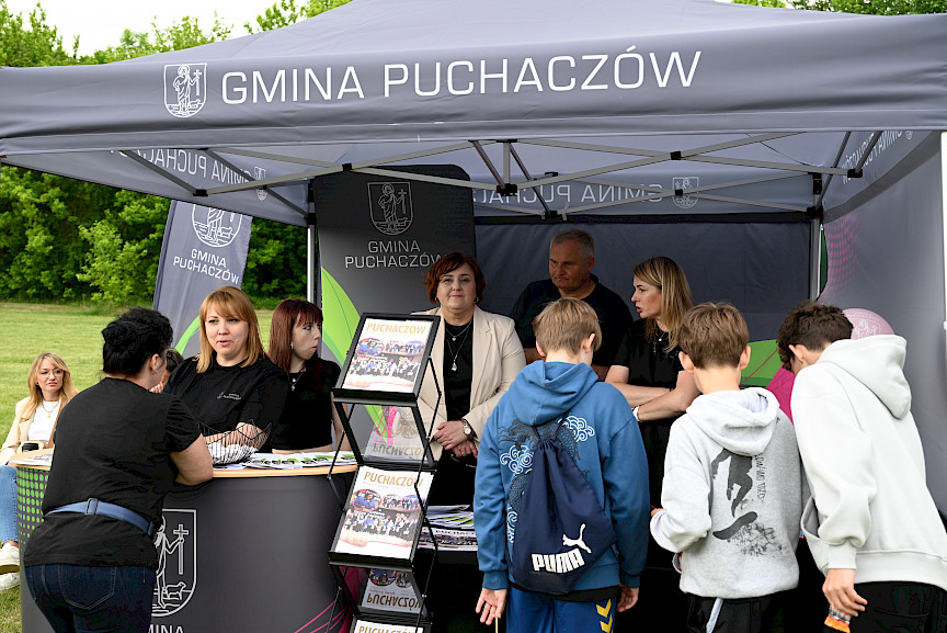 Stoisko Gminy Puchaczów i ludzie stojący za i przed stoiskiem.
