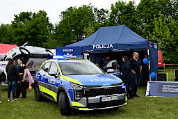 Stoisko policji, samochód policyjny, ludzie chodzący wokół i przyglądający się.