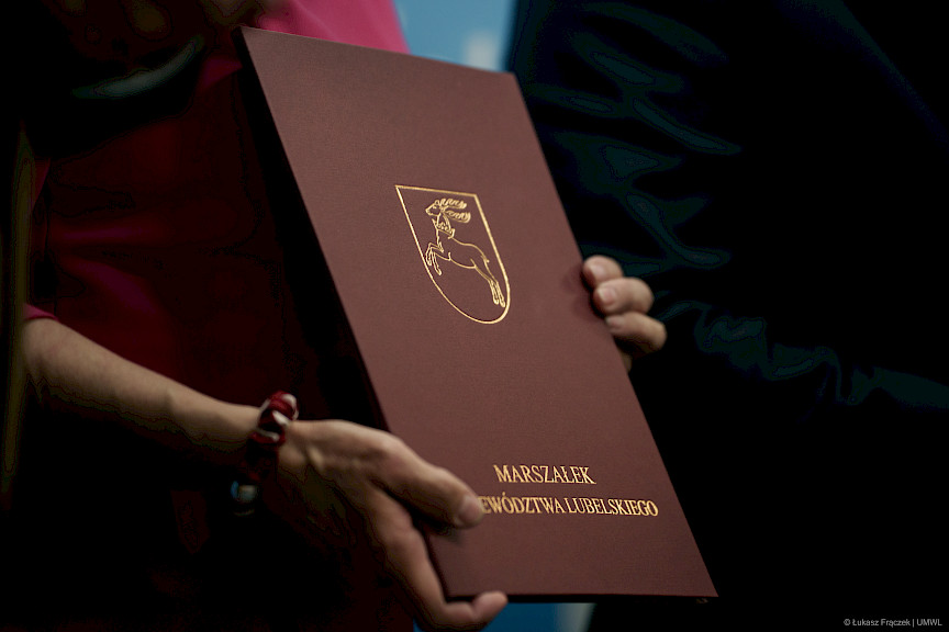 Ujęcie dłoni trzymających teczkę w kolorze bordowym, na okładce widnieje złoty napis Marszałek Województwa Lubelskiego oraz symbol województwa koziołek.