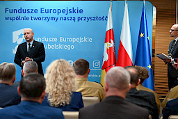 Wicemarszałek Województwa Lubelskiego przemawia ze sceny do publiczności. Za nim stoi ścianka promująca Fundusze Europejskie oraz flagi, Polską, Unii Europejskiej i Województwa Lubelskiego.