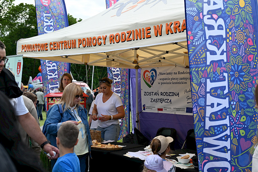 Stoisko Powiatowego Centrum Pomocy Rodzinie w Kraśniku, w środku panie, przed stoiskiem chłopiec