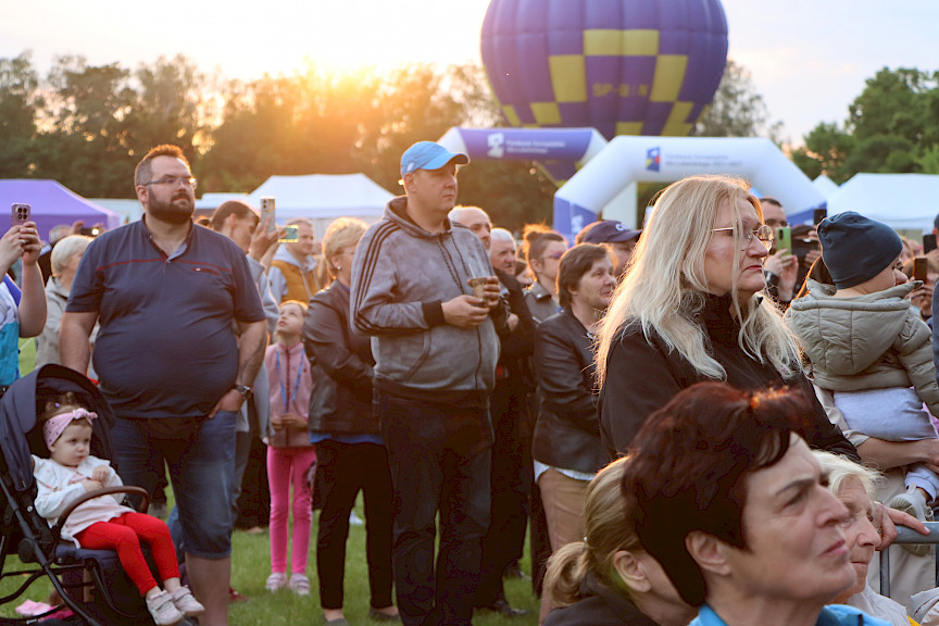 Tłum ludzi na pikniku, w tle balon i zachód słońca
