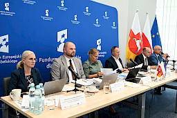 Dyrekcja Departamentu Zarządzania Programami Regionalnymi oraz przedstawiciele Departamentu Europejskiego Funduszu Rozwoju Regionalnego siedzący za stołem. Na stole znajdują się dokumenty, laptopy, mikrofonu, woda