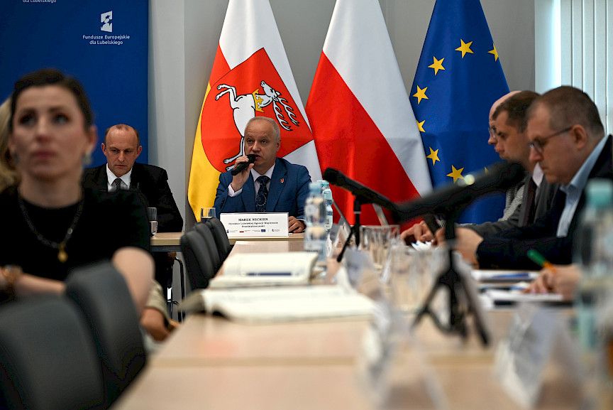 Widok z daleka na Dyrektora Lubelskiej Agencji Wspierania Przedsiębiorczości wypowiadająca się do mikrofonu. Bliżej widoczni są inni uczestnicy siedzący na sali.