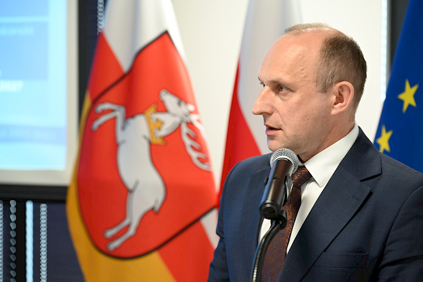 Ujęcie twarzy z bliska Dyrektora Departamentu Wdrażania Europejskiego Funduszu Rozwoju Regionalnego Andrzeja Danaja wypowiadającego się do mikrofonu.