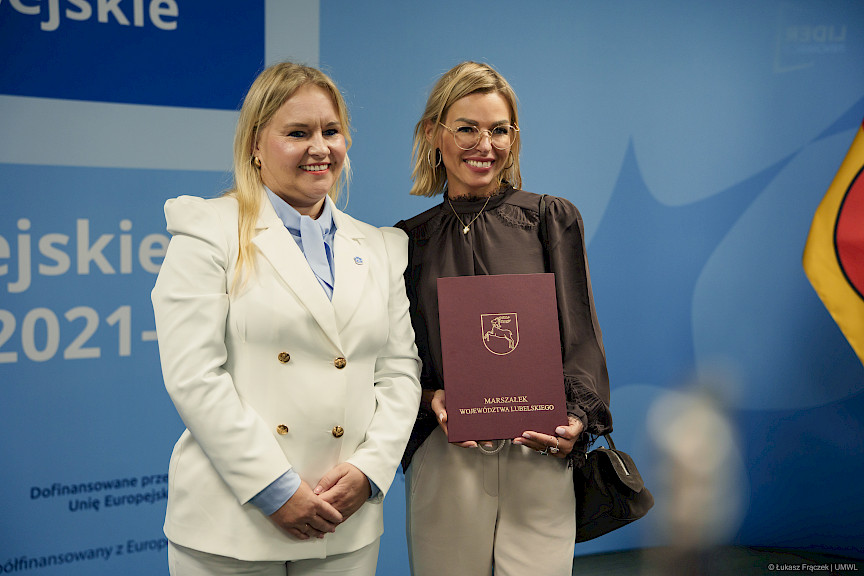 Dyrektor Departamentu Zarządzania Programami Regionalnymi Anna Brzyska stoi z beneficjentką projektu. Obie uśmiechają się szeroko.