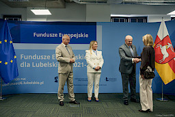 Marszałek Województwa Lubelskiego Jarosław Stawiarski podaje rękę w ramach gratulacji beneficjentce projektu. Obok stoją i patrzą na nich Dyrektor Anna Brzyska oraz Dyrektor LAWP Marek Neckier.