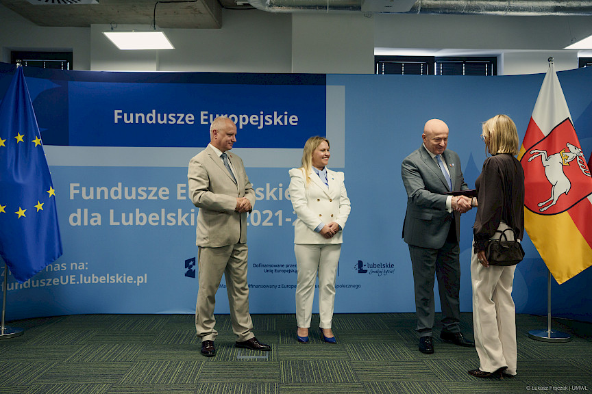 Marszałek Województwa Lubelskiego Jarosław Stawiarski podaje rękę w ramach gratulacji beneficjentce projektu. Obok stoją i patrzą na nich Dyrektor Anna Brzyska oraz Dyrektor LAWP Marek Neckier.