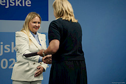 Dyrektor Departamentu Zarządzania Programami Regionalnymi Anna Brzyska podaje rękę w ramach gratulacji beneficjentce projektu, która odwrócona jest plecami do obiektywu.