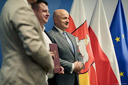 Marszałek Województwa Lubelskiego Jarosław Stawiarski ustawiony jest do zdjęcia z beneficjentem projektu. Ujęcie z profilu.