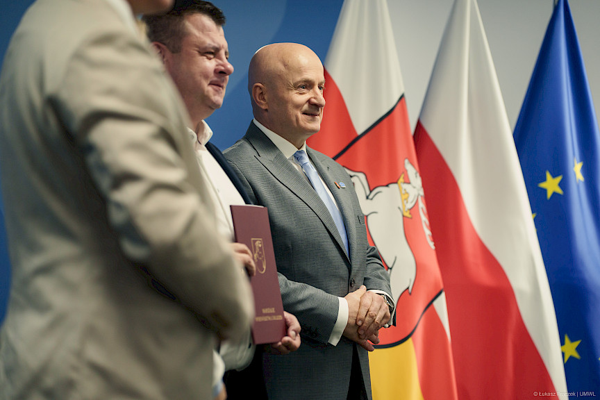 Marszałek Województwa Lubelskiego Jarosław Stawiarski ustawiony jest do zdjęcia z beneficjentem projektu. Ujęcie z profilu.