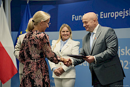 Marszałek Województwa Lubelskiego Jarosław Stawiarski podaje rękę w ramach gratulacji beneficjentce projektu. Za nimi widać Dyrektor Annę Brzyską, która szeroko uśmiecha się.