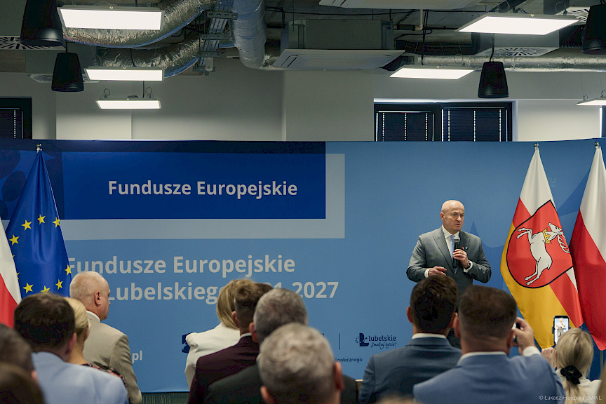 Marszałek Województwa Lubelskiego Jarosław Stawiarski przemawia do uczestników wydarzenia siedzących na sali. Za nim znajduje się ścianka promocyjna Funduszy Europejskich dla Lubelskiego.
