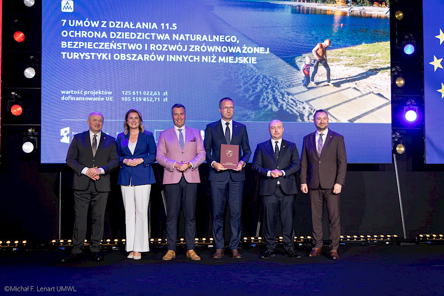 Zdjęcie Zarządu Województwa Lubelskiego z beneficjentem projektu, który trzyma w rękach bordową teczkę z umową.