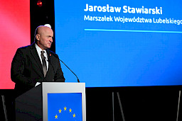 Marszałek Województwa Lubelskiego Jarosław Stawiarski przemawia do mikrofonu. Za nim wyświetlane jest na ekranie LED jego imię i nazwisko.