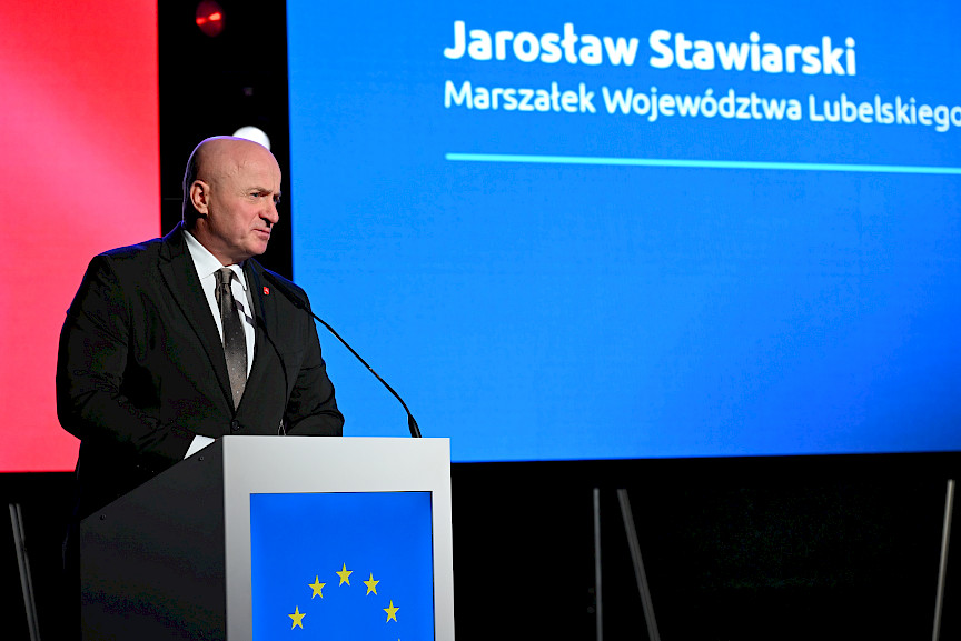 Marszałek Województwa Lubelskiego Jarosław Stawiarski przemawia do mikrofonu. Za nim wyświetlane jest na ekranie LED jego imię i nazwisko.