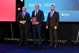 Marszałek Województwa Lubelskiego Jarosław Stawiarski z Wicemarszałkiem Markiem Wojciechowskim stoją z beneficjentem, który trzyma bordową teczkę w umową.