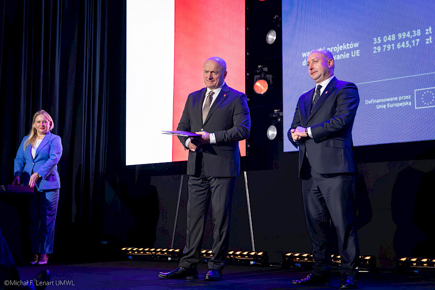Marszałek Województwa Lubelskiego Jarosław Stawiarski z Wicemarszałkiem Piotrem Bresiem czekają na podejście beneficjenta projektu. Marszałek Jarosław Stawiarski trzyma teczkę w umową.