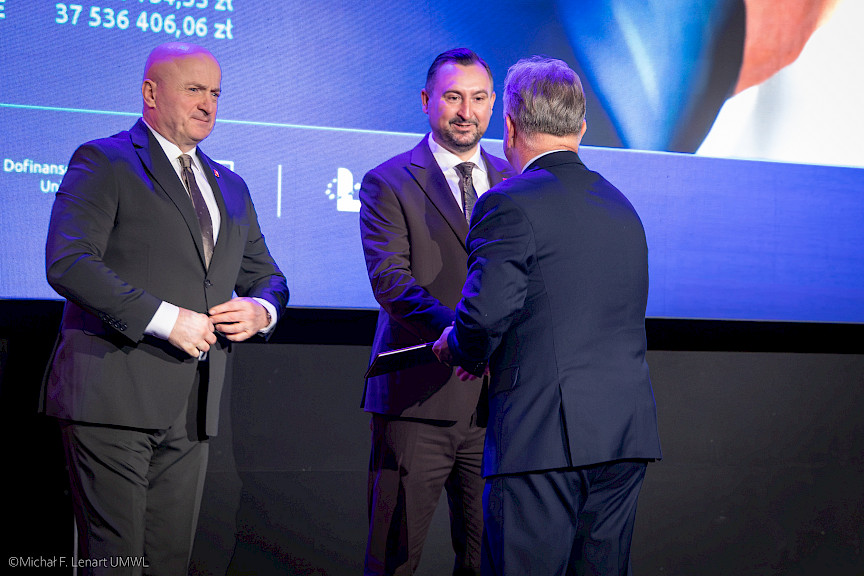 Wicemarszałek Marek Wojciechowski podaje rękę beneficjentowi projektu w ramach gratulacji. Obok stoi Marszałek Jarosław Stawiarski.