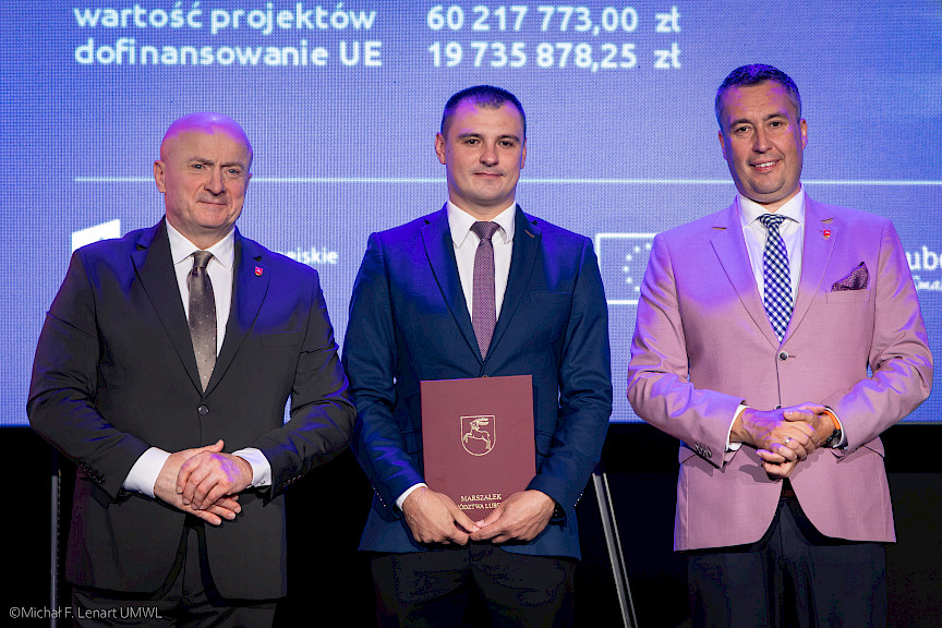 Marszałek Województwa Lubelskiego Jarosław Stawiarski wraz z Członkiem Zarządu Marcinem Szewczakiem stoją z beneficjentem projektu.