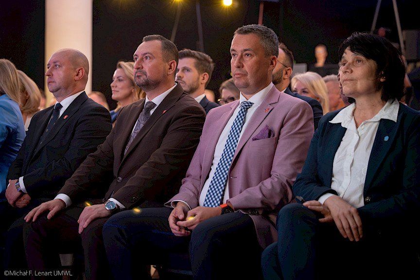 Ujęcie na Wicemarszałków Piotra Bresia, Marka Wojciechowskiego oraz Członka Zarządu Marcina Szewczaka siedzących na widowni z innymi uczestnikami wydarzenia.