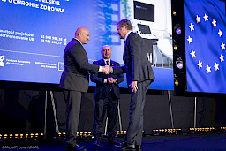 Marszałek Województwa Lubelskiego Jarosław Stawiarski podaje rękę beneficjentowi projektu w ramach gratulacji. Obok nich stoi Wicemarszałek Piotr Breś.