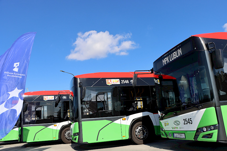 Ujęcie na trzy autobusy  ustawione na placu obok siebie pod skosem. Są w kolorach zielonym, czarnym i białym