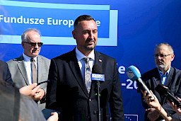 Wicemarszałek Województwa Lubelskiego Marek Wojciechowski udziela wywiadu mediom do mikrofonów. Za nim stoi dwóch mężczyzn.