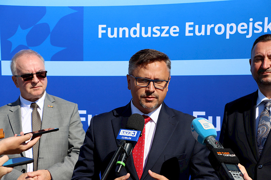 Prezes MPK Lublin Bogdan Kołciuk udziela wywiadu mediom do mikrofonów. Obok niego stoi Wicemarszałek Marek Wojciechowski oraz inny mężczyzna.