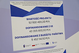 Ujęcie tablicy informacyjnej z liczbami przedstawiającymi wartość projektu i poziom dofinansowania z UE oraz budżetu państwa.