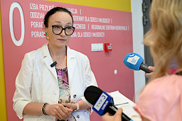 Kobieta z białym fartuchu udziela wywiadu mediom do mikrofonów.