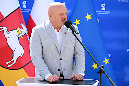 Marszałek Województwa Lubelskiego Jarosław Stawiarski wypowiada się do mikrofonu do uczestników spotkania. Za nim widoczne są flagi, unii europejskiej, polski oraz województwa lubelskiego