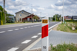 Zdjęcie fragmentu drogi, w koło widoczne są budynki. Na pierwszym planie widnieje słupek z numerem drogi 833.