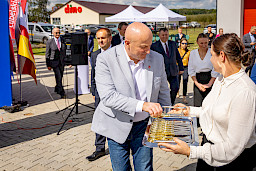 Marszałek Województwa Lubelskiego Jarosław Stawiarski bierze ze srebrnej tacy nożyczki do przecięcia wstęgi. Tacę trzyma kobieta w białej bluzce, w koło widoczne są inne osoby.