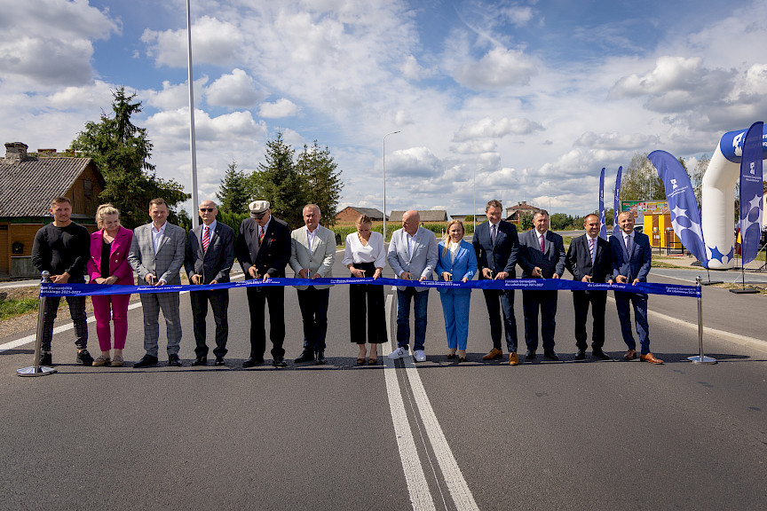 Ujęcie grupy osób ustawionych obok siebie, wszyscy trzymają nożyczki w ręku, są przed przecięciem symbolicznej wstęgi otwierającej drogę. Po środku stoi Marszałek Jarosław Stawiarski oraz Dyrektor Anna Brzyska.