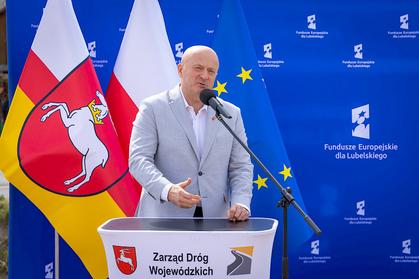 Marszałek Województwa lubelskiego Jarosław Stawiarski wypowiada się do mikrofonu do uczestników wydarzenia. Za nim stoi niebieska ścianka promująca fundusze europejskie dla lubelskiego..