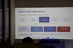 Pod sufitem na dużym ekranie wyświetlona jest informacja co zmieniło się w szpitalu po wprowadzeniu systemu cyfryzacji.